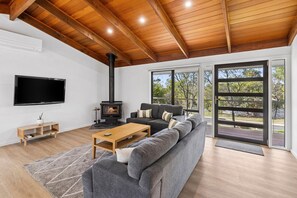 A modern living room with a large gray sectional sofa, a wooden coffee table, a black fireplace, and a flat-screen TV mounted on the wall. - Nod Off On Noble (Anglesea)