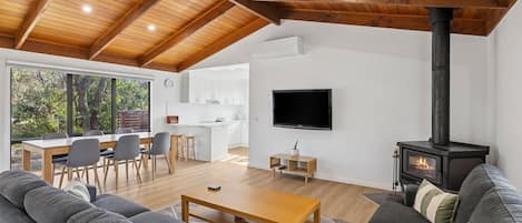 A modern living room with a fireplace, a television, and a dining area with a kitchen in the background.
