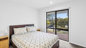 A bedroom with a large bed, a nightstand, a lamp, and a sliding glass door leading to an outdoor area.