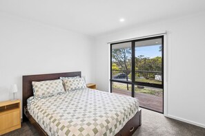 A bedroom with a large bed, a nightstand, a lamp, and a sliding glass door leading to an outdoor area. - Nod Off On Noble (Anglesea)