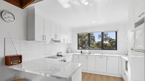 A modern kitchen with white cabinetry, a marble countertop, and a window providing a view of trees.