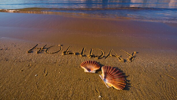 Una spiaggia con la scritta "HOLIDAY" sulla sabbia e due conchiglie.