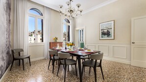 A dining area with a round table set for six, surrounded by six chairs. There is a chandelier above the table, and a painting on the wall to the right. - Ca' Mainella Grand Canal (Venice)