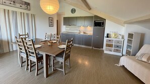 Une cuisine moderne avec des meubles gris, un four à micro-ondes et un évier. On y trouve un coin repas avec une table et des chaises en bois, ainsi qu’un grand luminaire suspendu.