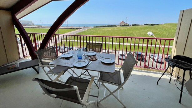 Un balcon avec une table dressée pour le dîner, donnant sur une pelouse et un plan d’eau.
