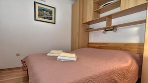 Een netjes opgemaakt bed met een roze dekbed, een houten hoofdbord en een plank erboven.