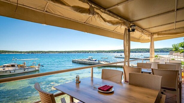 A covered outdoor seating area with a view of the sea and boats.