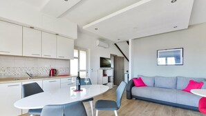 Una cucina moderna con mobili bianchi, un tavolo da pranzo con sedie e un divano grigio con cuscini rossi.