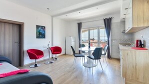Una camera d'albergo moderna con zona pranzo, angolo cottura e un'ampia finestra con tende.
