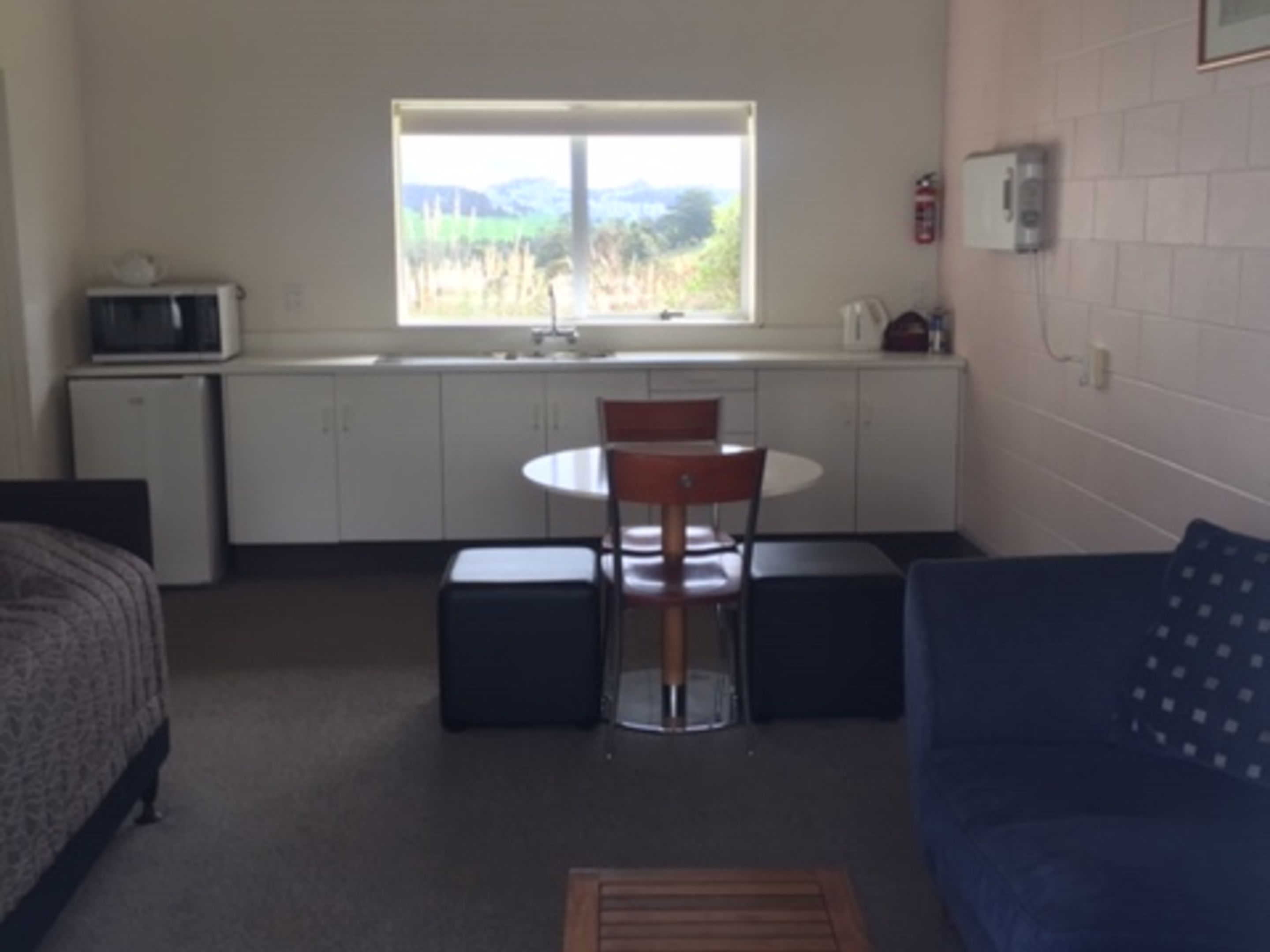 A compact room with a kitchenette, a dining table with chairs, a sofa, and a window with a view of the outdoors.