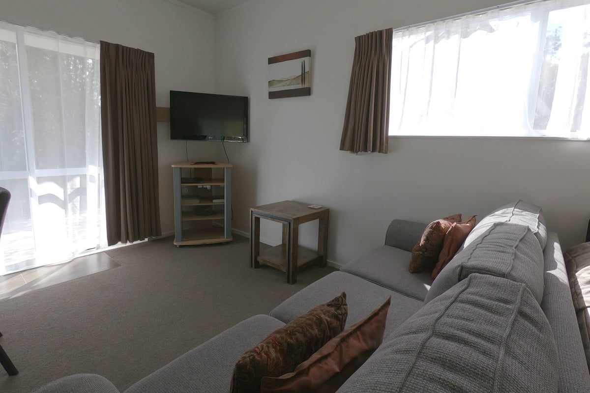A living room with a sofa, a TV on a stand, a small table, and a window with curtains.