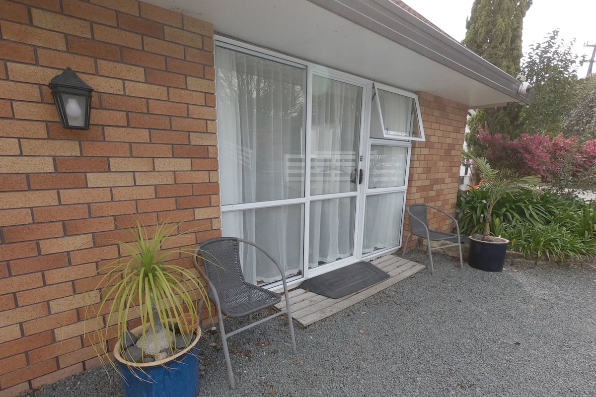 A house with a brick exterior, a sliding glass door, a potted plant, and a chair outside.