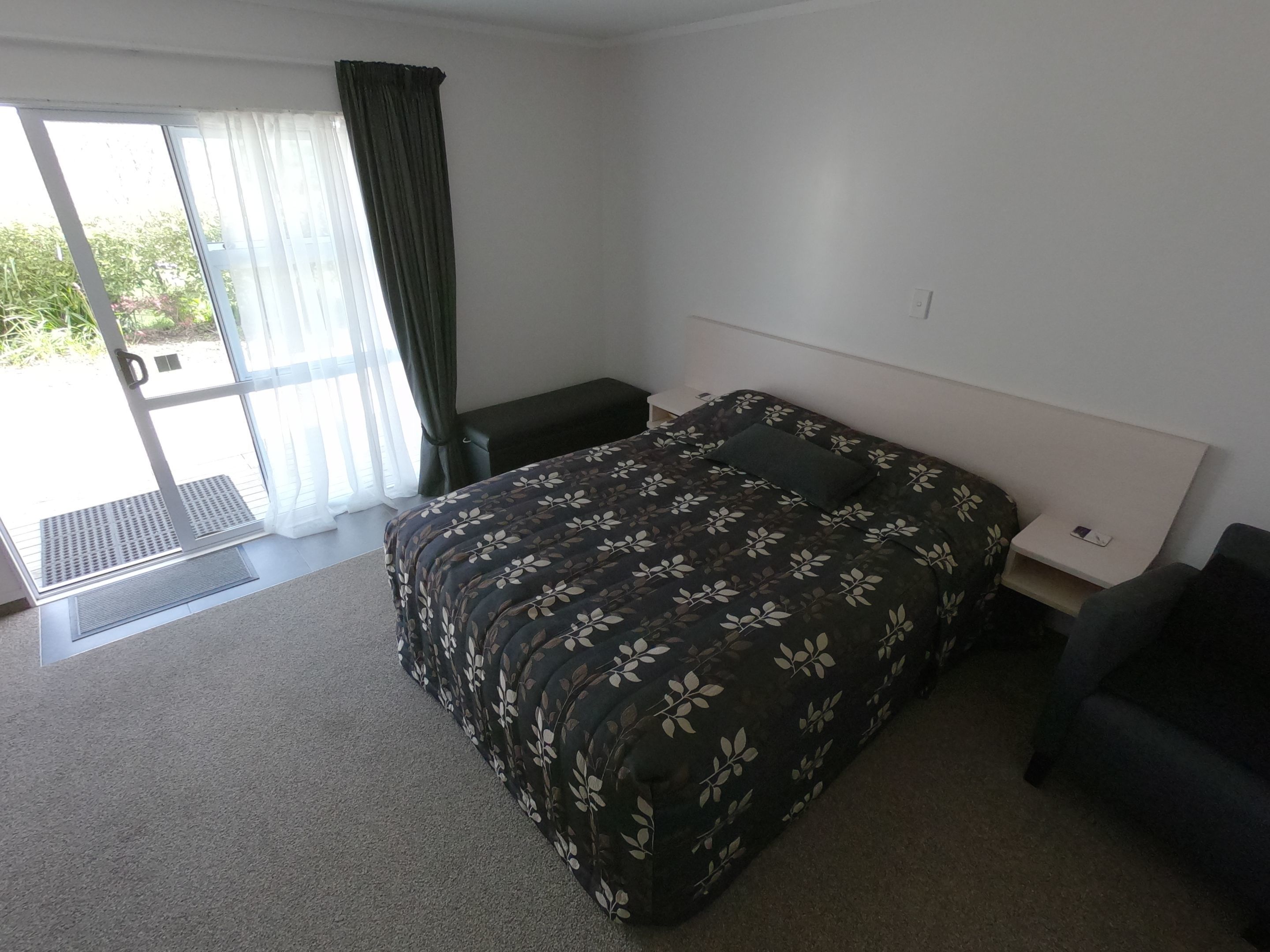 A bedroom with a bed, a nightstand, a bench, and a sliding glass door leading to a balcony.