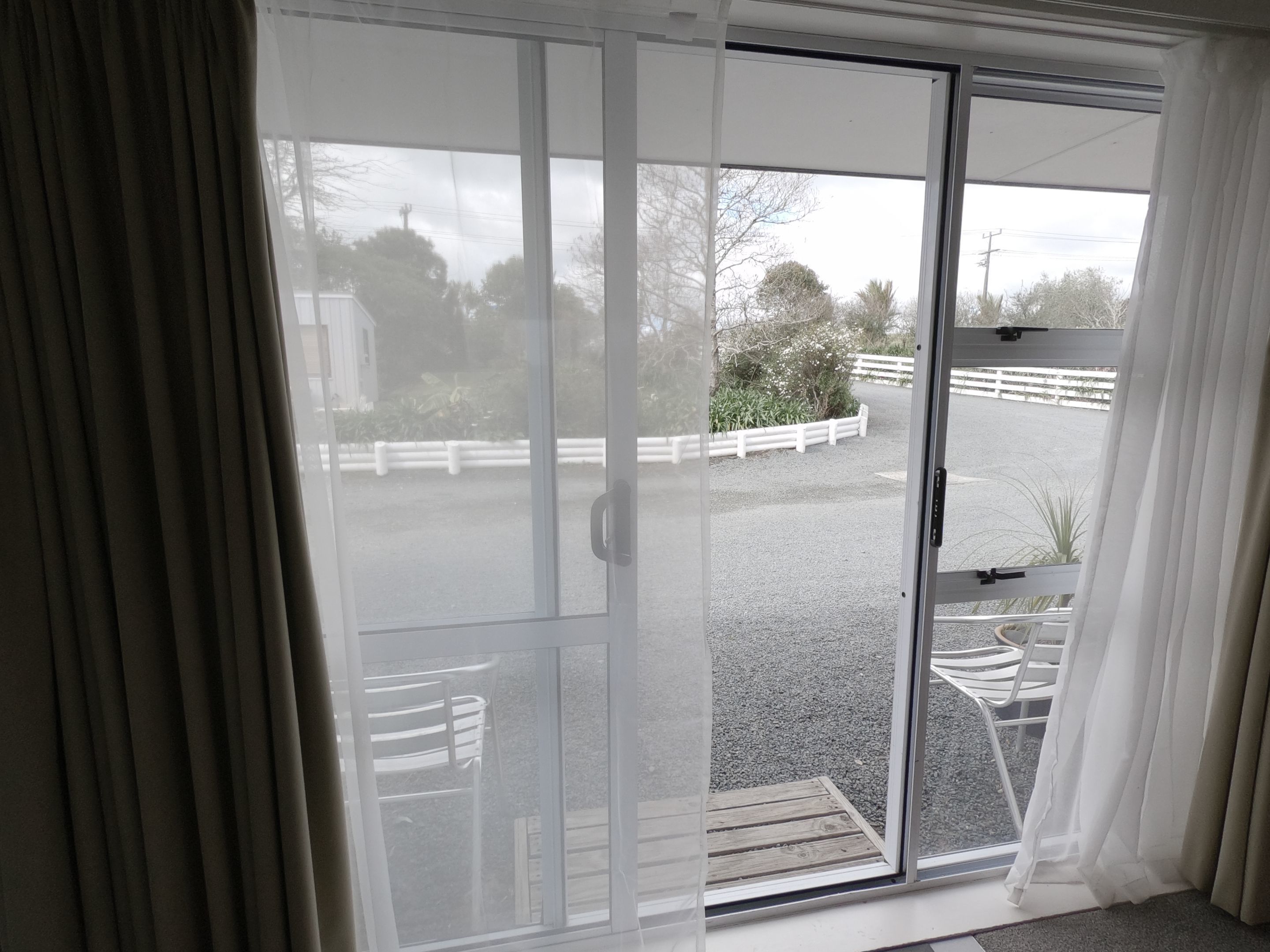 A room with a sliding glass door leading to an outdoor area with a gravel path, white fence, and chairs.