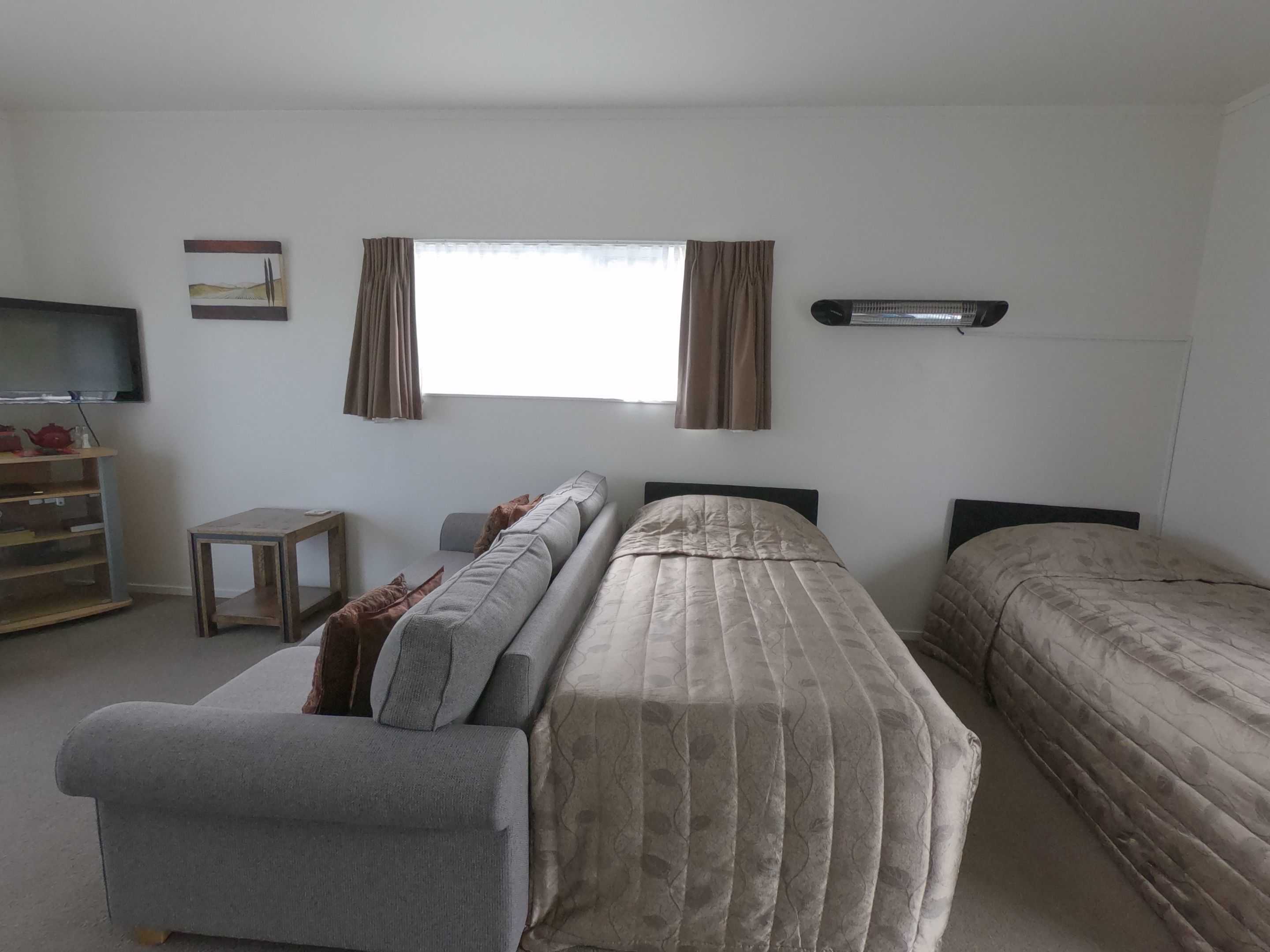 Una stanza con un divano, un letto, un tavolino, una televisione e una finestra con tende.