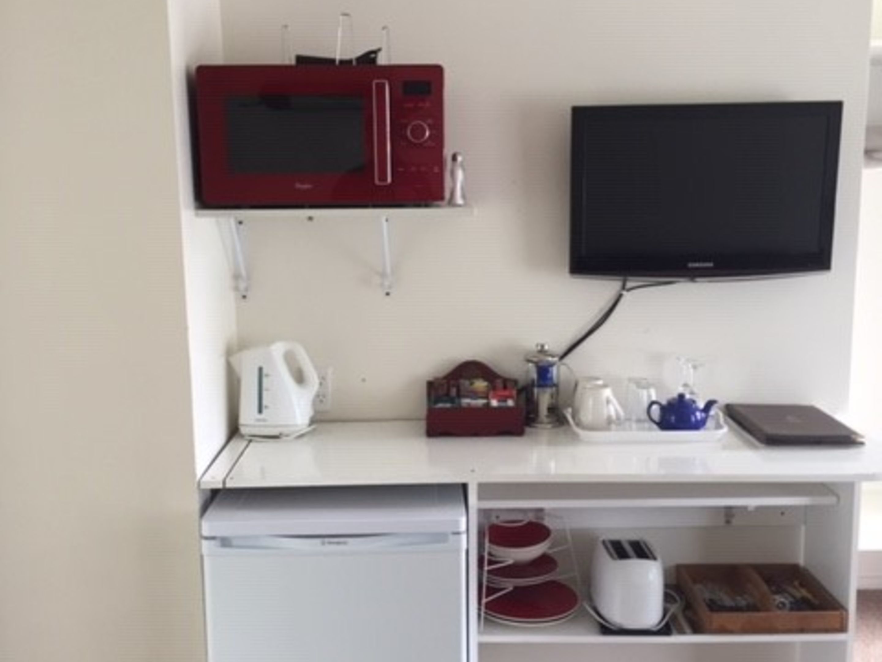 A kitchenette with a microwave, toaster, kettle, and a flat-screen TV mounted on the wall.