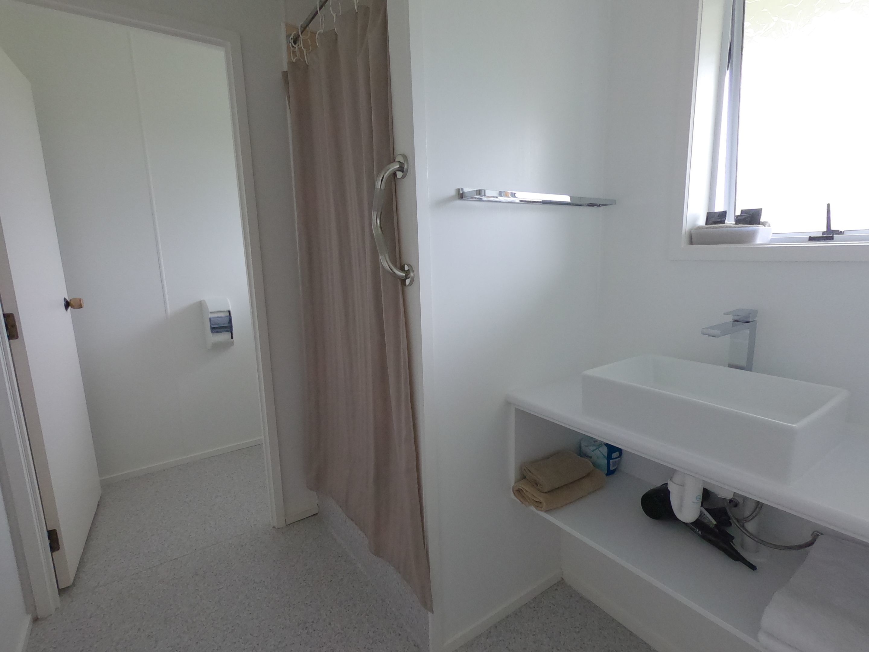 A bathroom with a shower curtain, a sink, and a window.