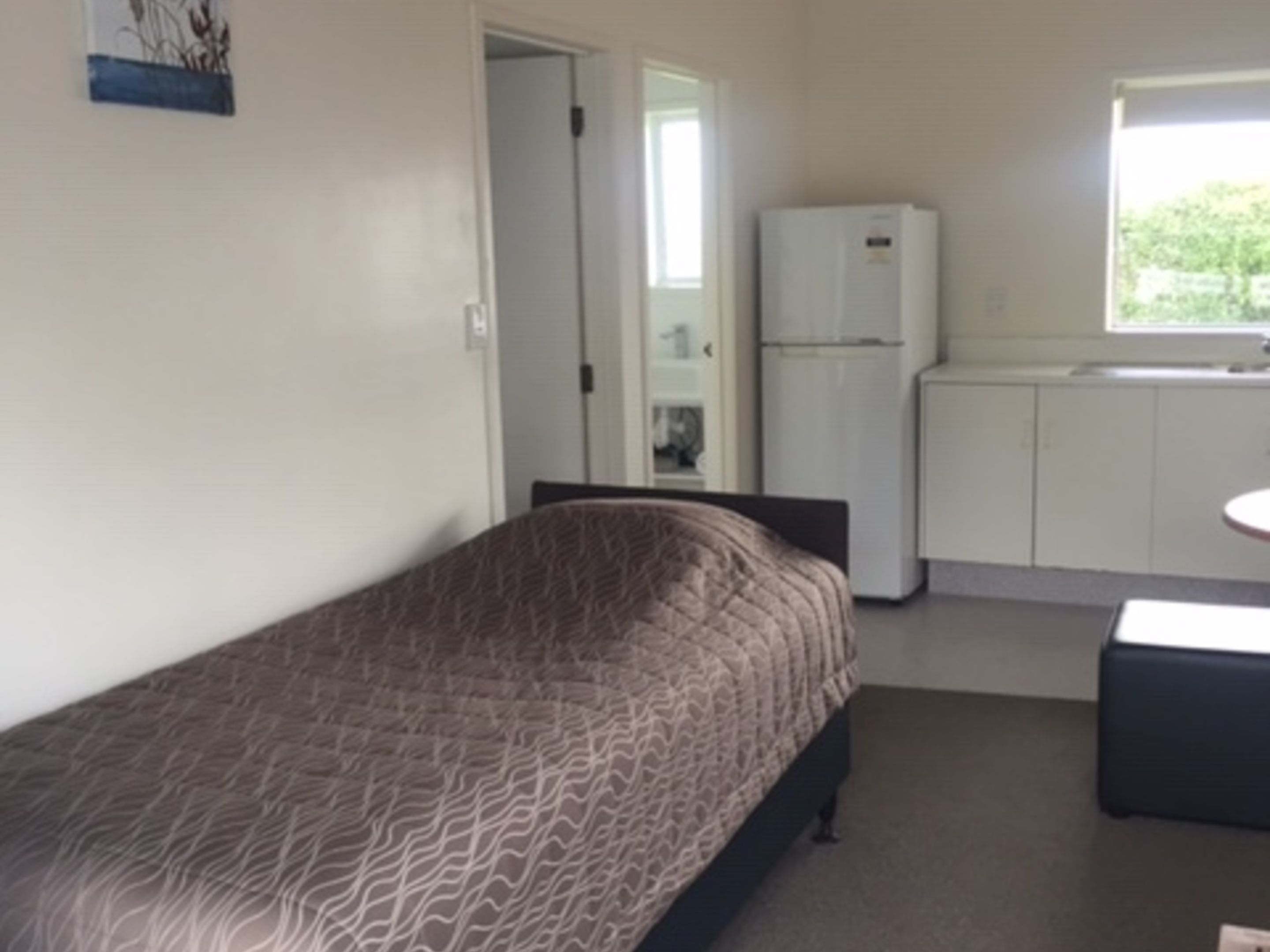 Un dormitorio con cama, un escritorio pequeño, un refrigerador y una ventana.