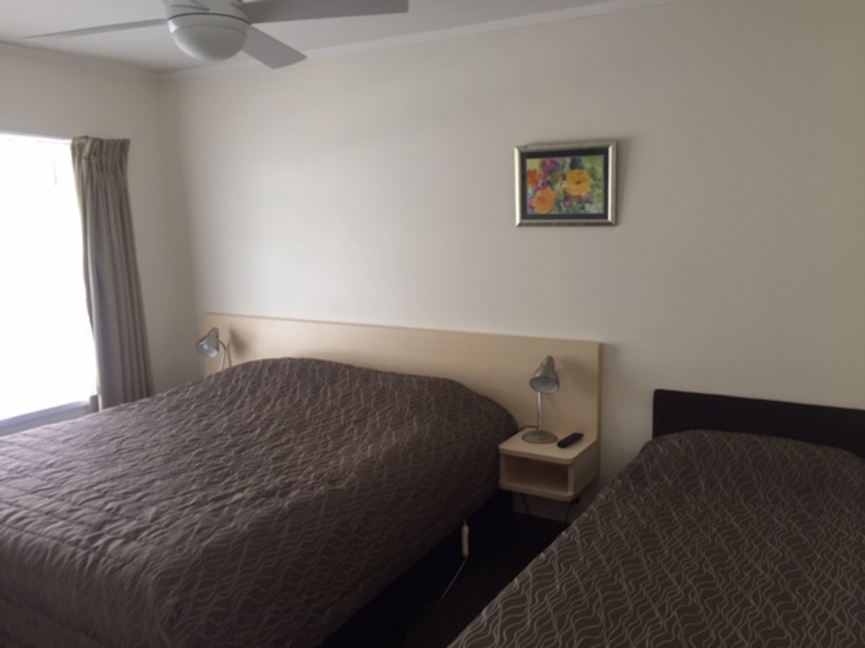 A hotel room with two beds, a ceiling fan, a nightstand with a lamp, and a framed picture on the wall.