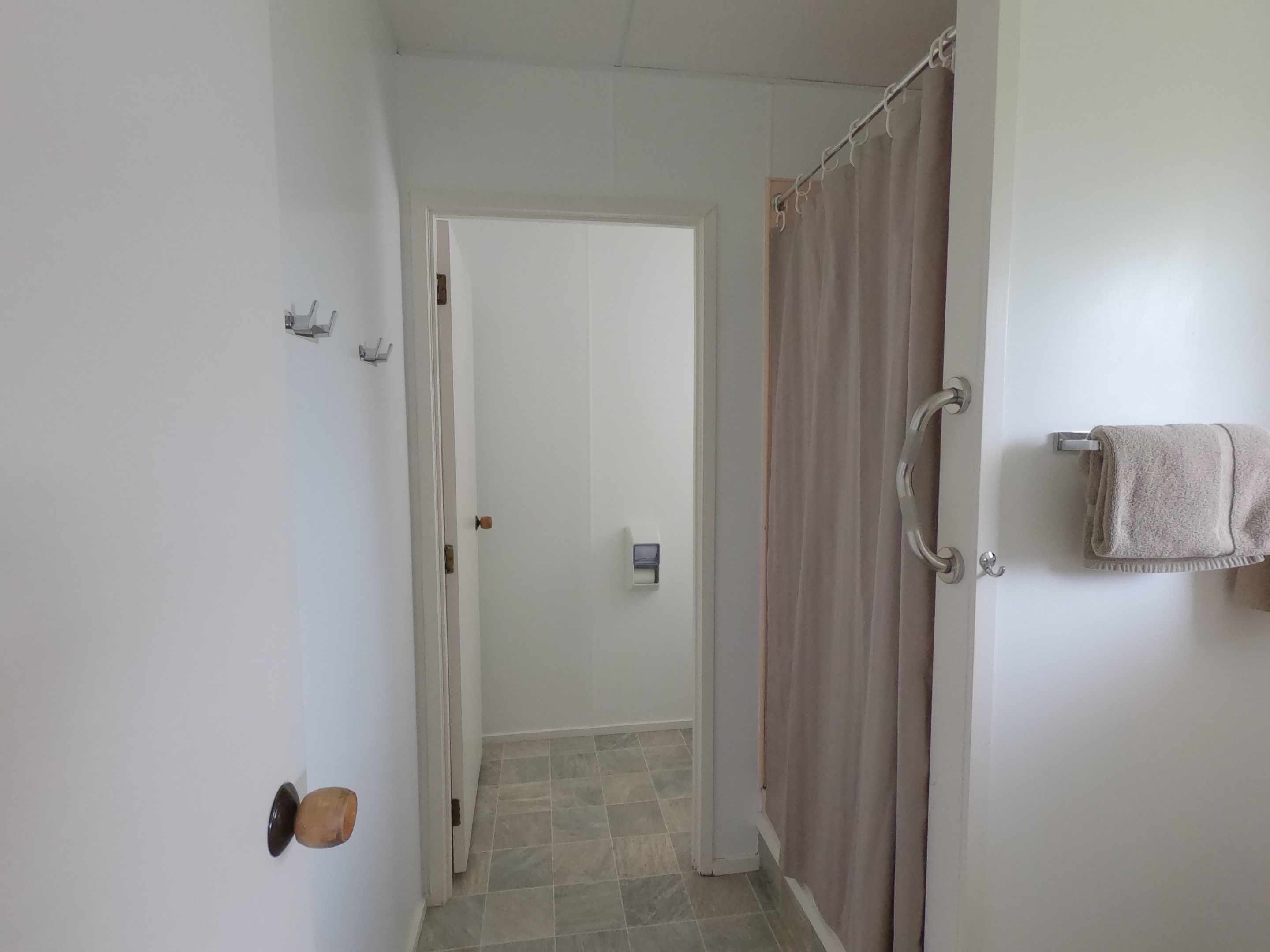 A bathroom with a shower curtain, a towel rack, and a door leading to another room.