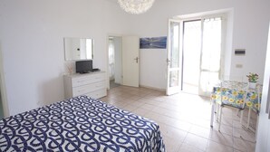 A bedroom with a bed, a dresser, a television, a chandelier, a painting, and a balcony with a table and chairs.