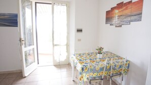 A dining area with a table covered in a floral tablecloth, white chairs, and a potted plant.