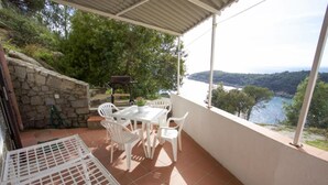 A covered patio with a table and chairs, overlooking a body of water and hills.