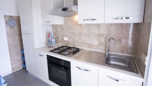 A modern kitchen with white cabinets, a gas stove, a stainless steel sink, and a built-in oven.
