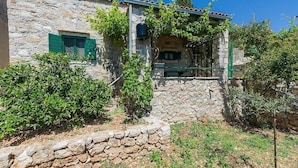 Un bâtiment en pierre à l’aspect rustique, doté d’une petite fenêtre avec des volets verts et d’un mur en pierre à l’avant.