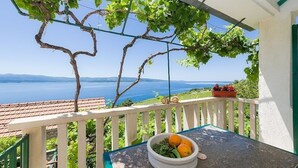 Un balcon avec une table, un panier de fruits et une vue sur la mer et les montagnes.
