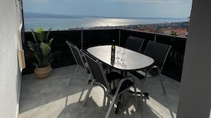 A balcony with a table and chairs, a potted plant, and a view of the sea and distant buildings. - Apartment in Crikvenica with Seaview, Balcony, Air condition, WIFI (3492-7) (Crikvenica)
