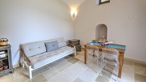 Una habitación con sofá, una mesa de madera con sillas, un armario pequeño y un aplique de pared.