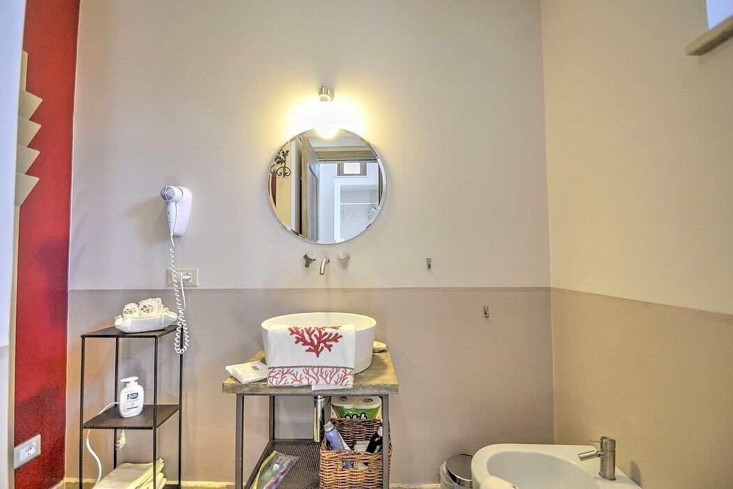 A bathroom with a round mirror, a hairdryer, a sink, and a shelf with toiletries.