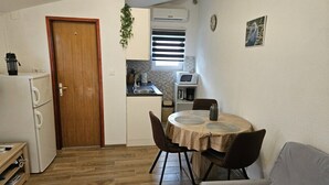 Un espace de vie compact comprenant un coin cuisine, un coin repas avec une table ronde et des chaises, et un canapé.