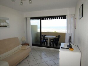 Relax on the balcony with a beach view, featuring a sofa, table, and desk with TV.