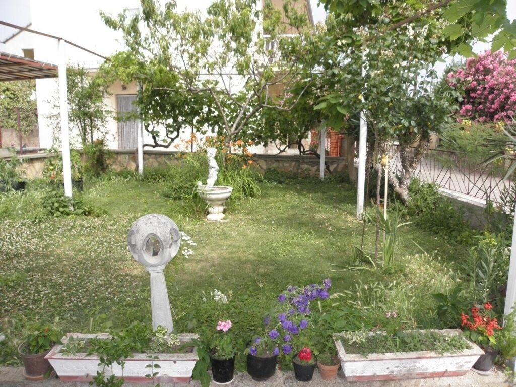 A garden with a fountain, potted plants, and a pergola.