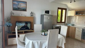 A living room with a television, a dining table with chairs, a kitchen area with cabinets and a window, and a decorative wall piece. - Apartment in Lumbarda with Seaview, Terrace, Air condition, WIFI (128-1) (Lumbarda)