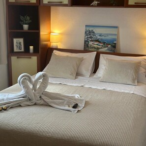 A neatly made bed with a towel arranged in a swan shape, a painting of a coastal scene, and a bedside lamp. - Apartment in Lumbarda with Seaview, Terrace, Air condition, WIFI (128-1) (Lumbarda)