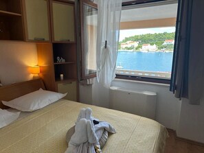 A hotel room with a bed, a bedside table with a lamp, a window with a view of the sea, and a wardrobe. - Apartment in Lumbarda with Seaview, Terrace, Air condition, WIFI (128-1) (Lumbarda)