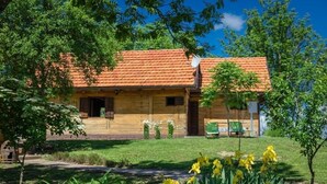A wooden house with a red-tiled roof, surrounded by greenery and yellow flowers.