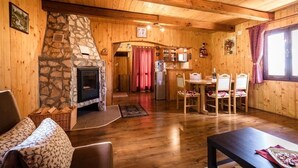 A cozy cabin interior with a stone fireplace, wooden walls, a dining area, and a kitchen.