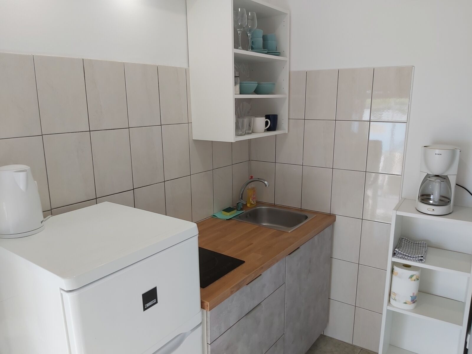 Cocina compacta con un refrigerador blanco, encimera de madera, un lavamanos y una cafetera Bosch.