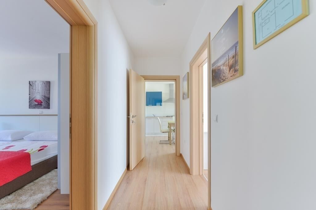 A narrow hallway with wooden flooring leading to a bedroom with a bed and a red blanket.