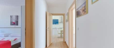 A narrow hallway with wooden flooring leading to a bedroom with a bed and a red blanket.
