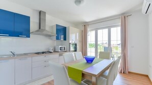 A modern kitchen with white cabinets, a built-in microwave, and a gas stove. There is a dining table with chairs and a blue bowl on the table. - Apartment in Vir with Terrace, Air condition, WIFI, Dishwasher (4589-1) (Vir)