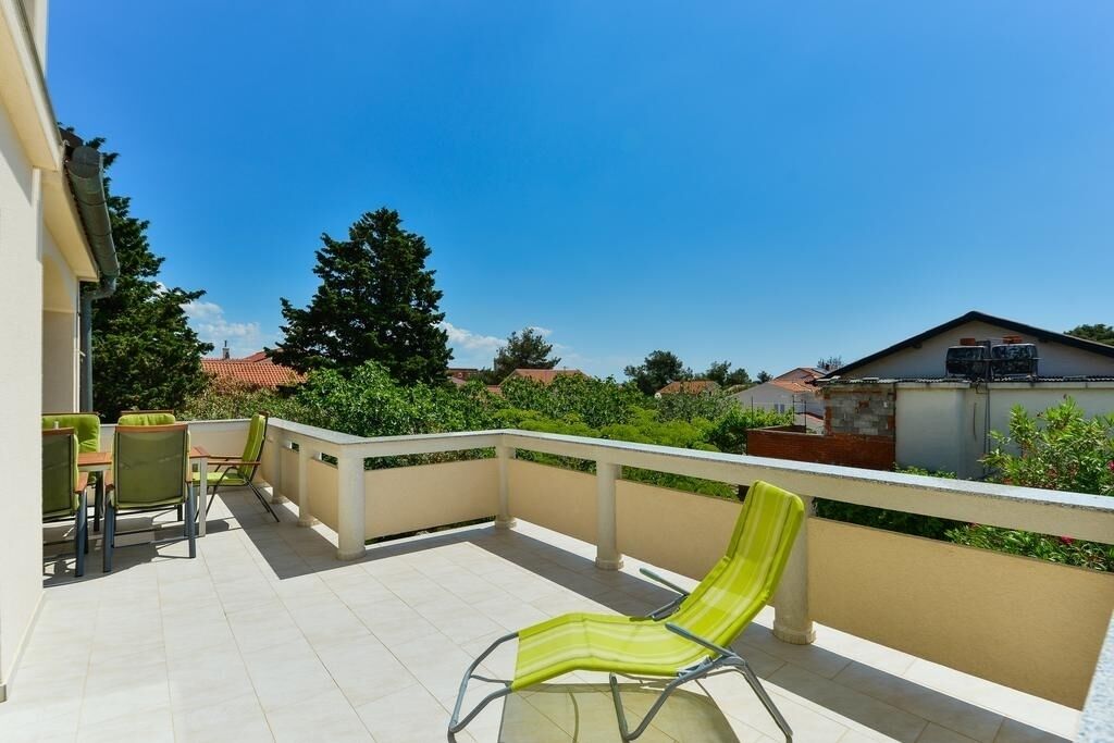 A balcony with a green chair, a table, and chairs.