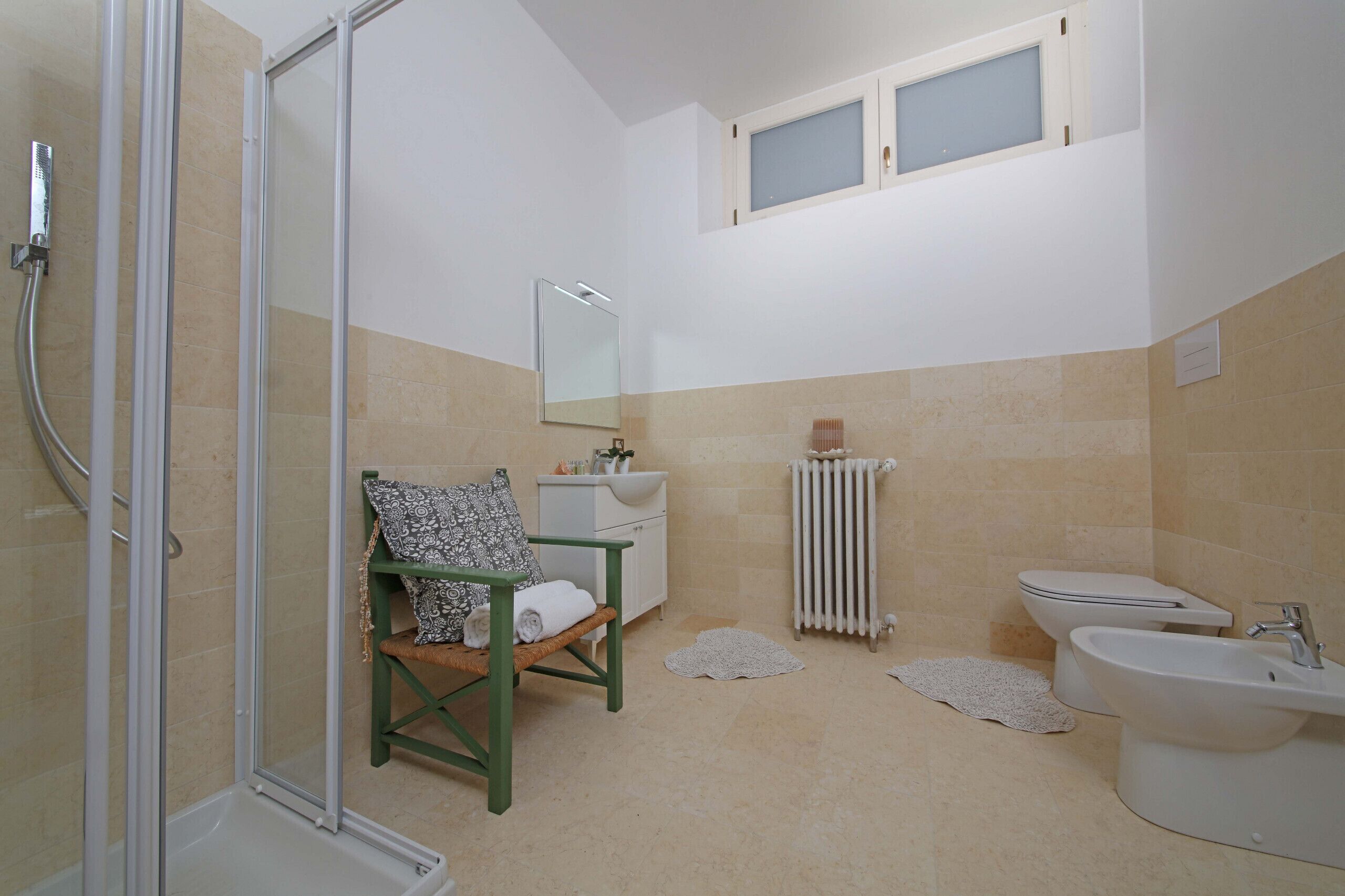 A bathroom with a shower, toilet, sink, and a chair with a towel.