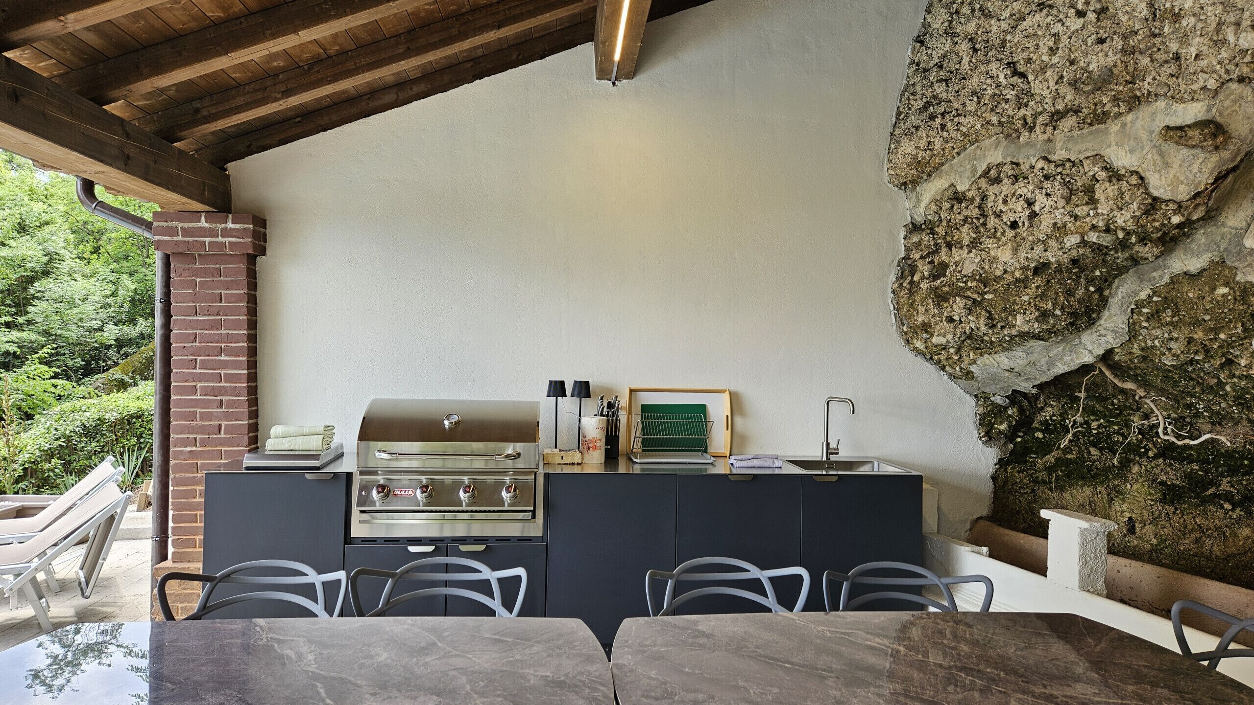 An outdoor kitchen with a grill, a sink, and a dining area with chairs and a table.
