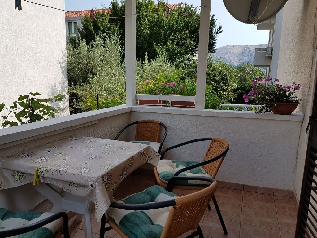 A balcony with a table and chairs, surrounded by potted plants and a view of greenery and mountains.