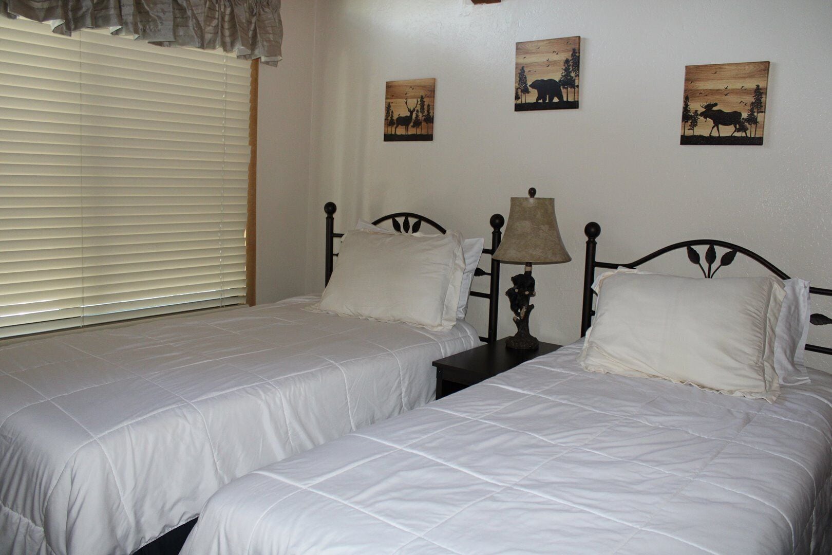 A bedroom with two beds, a nightstand with a lamp, and wall art depicting animals.